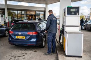 Werknemer tankt benzine bij pomp met prijskaart €2,14 en tekst reiskostenvergoeding €0,23 per kilometer 2026